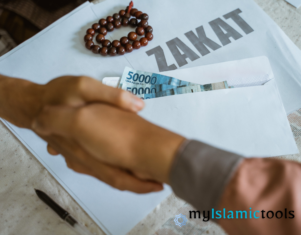 A smartphone displaying a Zakat calculator surrounded by gold coins, currency notes, and prayer beads on a white table.
